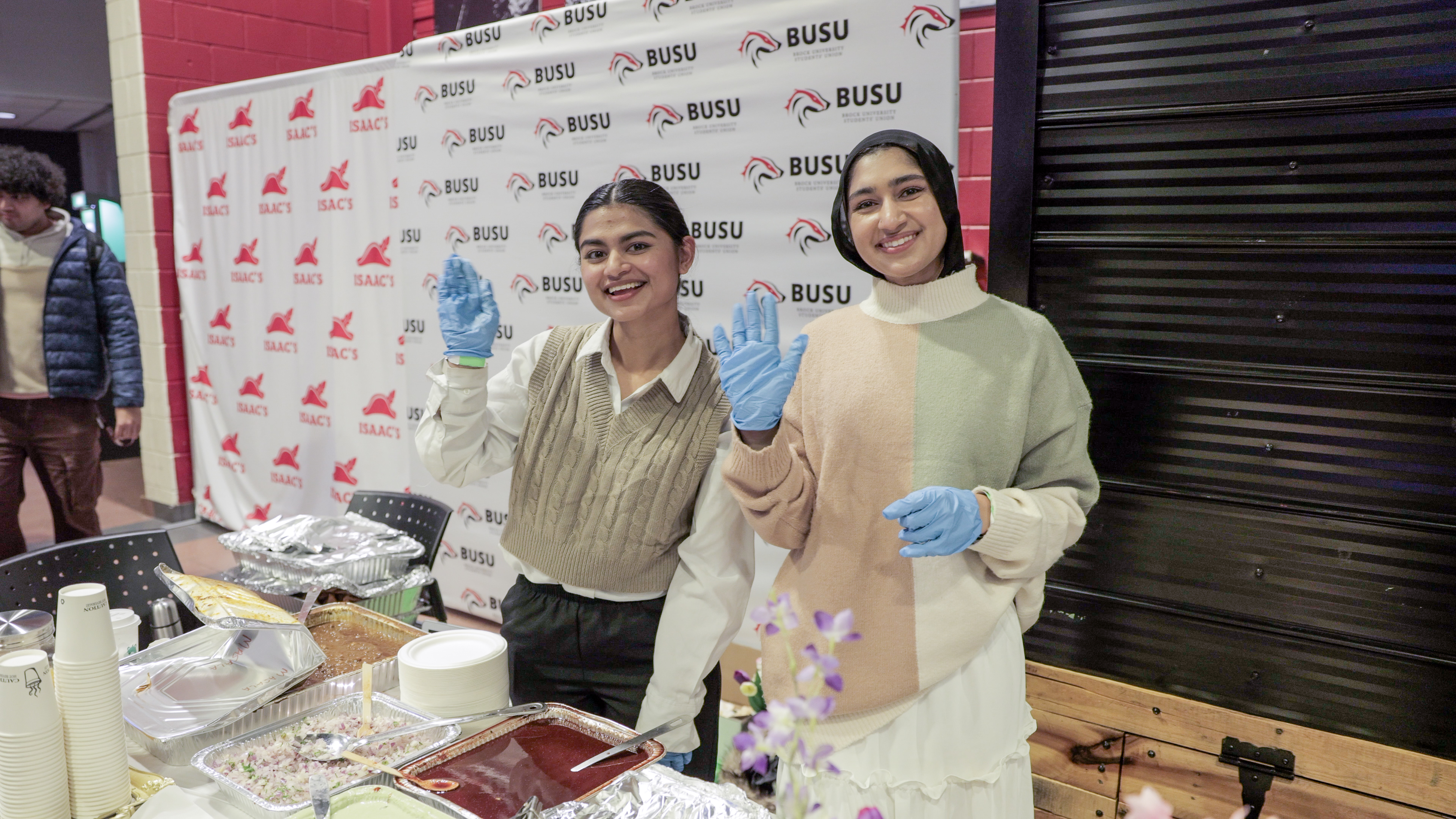 Two students at a club event waving at the camera