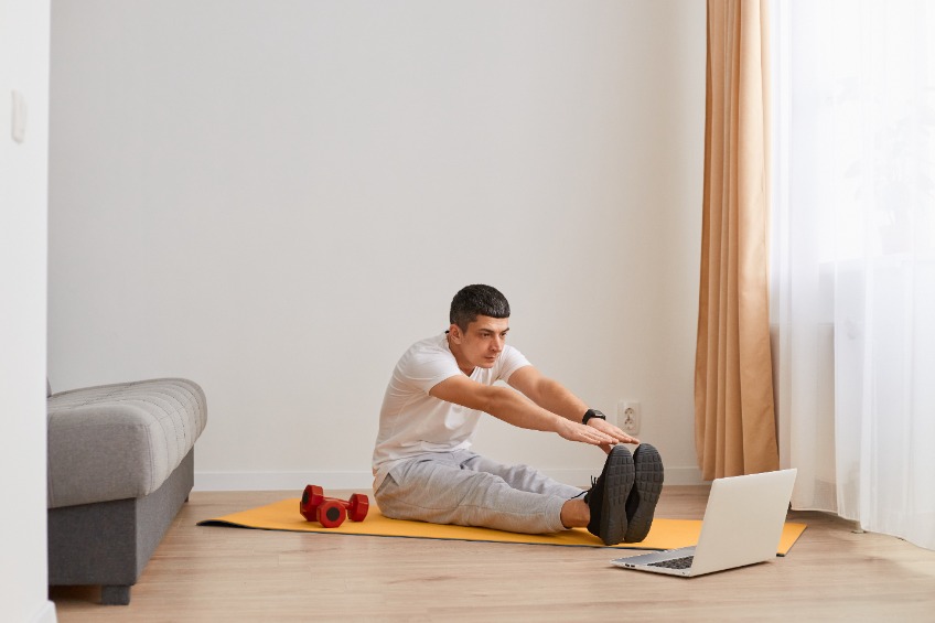 Student sitting on a yoga mat looking at laptop stretching his legs