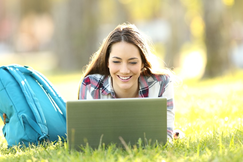 Student laying in the grass looking at laptop