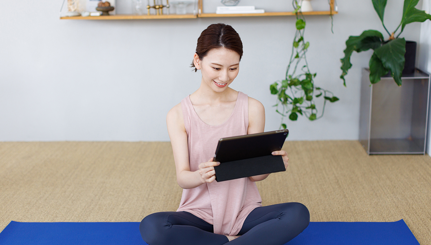 Young person sitting in a yoga studio smiling and looking at a tablet